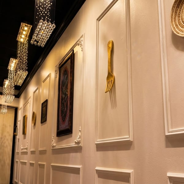 Elegant restaurant hallway with crystal chandeliers, framed art, and a large golden fork wall decoration.