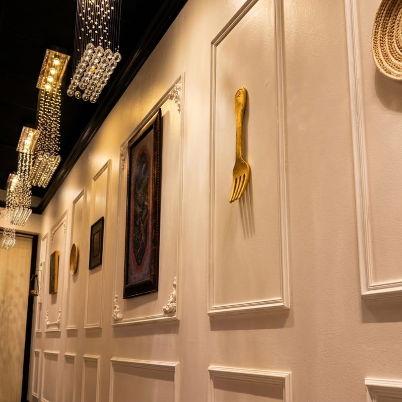 Elegant restaurant hallway with crystal chandeliers, framed art, and a large golden fork wall decoration.